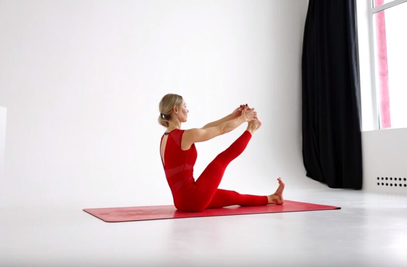  A woman in a red outfit conducts the Hamstring Test, a flexibility measurement exercise, as part of her progress tracking routine.