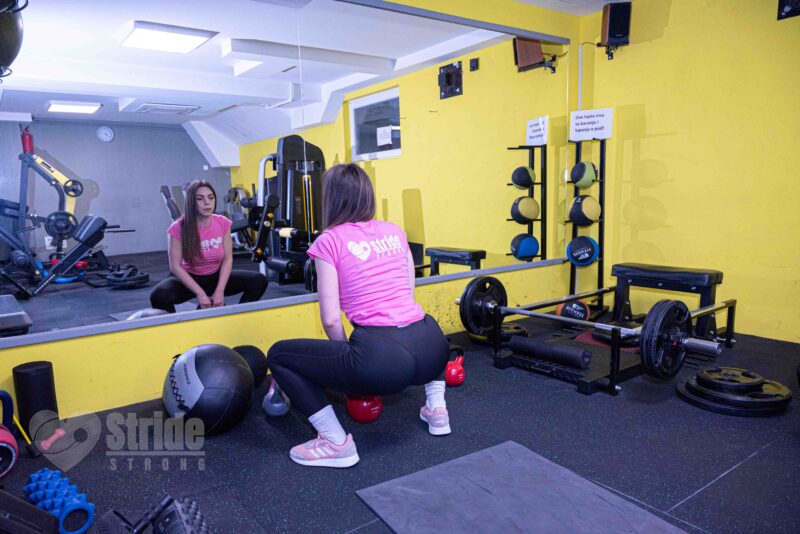 The girl is doing strength training - performing squats with Kettlebell
